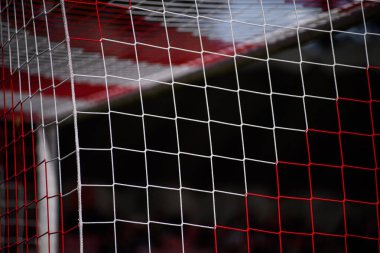 Köşesinde tekrarlanan kare ağ ile kırmızı ve beyaz futbol gol; minimalist spor dokusu ve geometri.