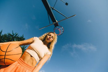 Basketbol potası altında sportif bir kadın, kararlı görünüyor, modern sokak sporu kavramı..