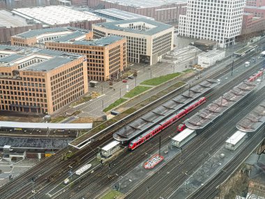 COLOGNE, GERMANY - 01 Ocak 2026: Bulutlu bir kış gününde Köln, Almanya 'da kırmızı tren, raylar ve MesseCity ofis blokları ile Koeln Messe Deutz istasyonunun genel görünümü.