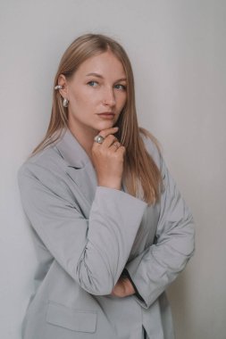 Beyaz bir duvara karşı duran, klasik gri ceketli sarışın bir iş kadınının portresi, düşünceli görünüyor. Bağımsızlar için ortak çalışma alanı. Uzaktan kumanda. Ofis çalışanı afişi.