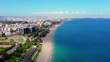 Aerial panoramic view of Antalyas coastline, showing the long sandy beach, turquoise Mediterranean Sea and sprawling cityscape under clear summer skies.