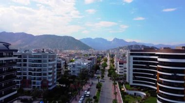 Antalya 'da bir yerleşim bölgesinden yükselen insansız hava aracı engebeli dağ sıralarının, modern binaların ve parlak gün ışığında ağaçlarla kaplı uzun bir caddenin çarpıcı manzarasını gözler önüne seriyor..
