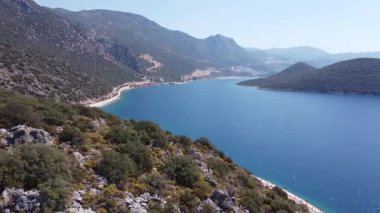Aerial panoramic view of Kas city with red rooftops, winding road, turquoise Mediterranean Sea and surrounding mountains. Travel destination and seaside lifestyle concept. Ungraded, DLog
