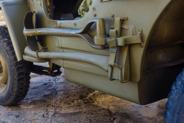Olive Drab Askeri Jeep 'in kayışlı, aletli ve çamur korumalı yakın çekimi.