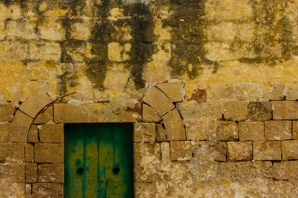 Yeşil kapılı ve yıpranmış mazoninin kemerli kadim sarı taş duvarı