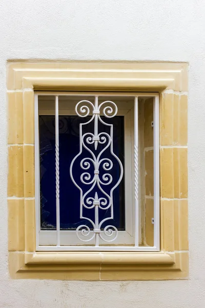 Beyaz duvarda bej taş çerçeveli beyaz demir pencere ızgarası