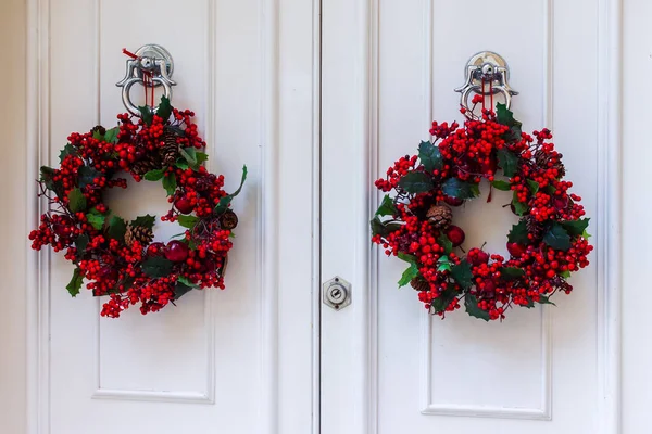 Beyaz Kapılarda İki Kırmızı Böğürtlen Noel Çelengi Bayram Dekorasyonu Oluşturdu