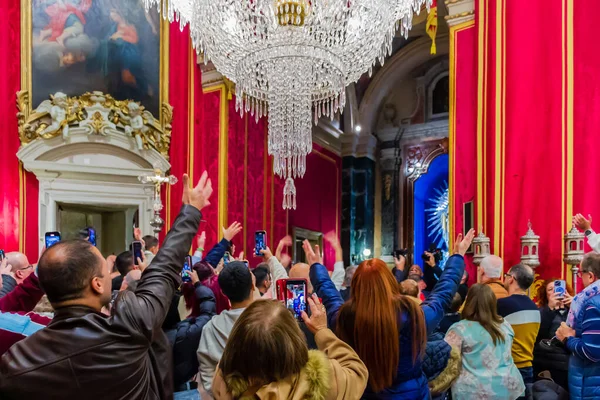 Cospicua, Malta - November 28th, 2025, Crowd of People Raising Phones in Opulent Red Velvet Hall Beneath Crystal Chandelier
