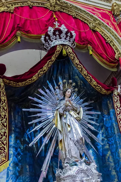 Cospicua, Malta - November 28th, 2025, Religious Statue of Virgin Mary with Radiant Halo and Ornate Robes on Velvet Backdrop
