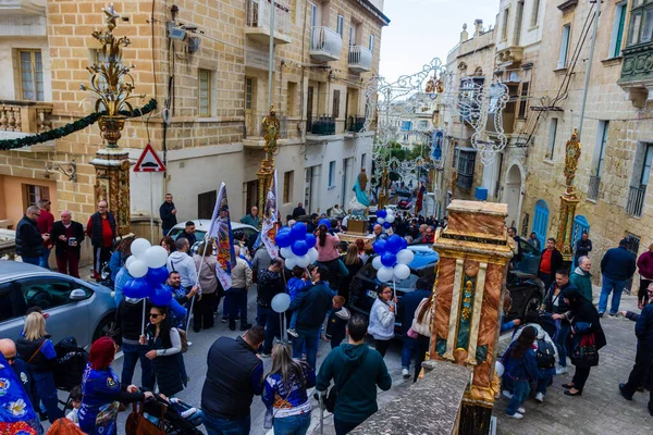 Cospicua, Malta - November 30th, 2025, Vibrant Street Parade With Blue And White Balloons, Flags, And Crowds Celebrating Festival