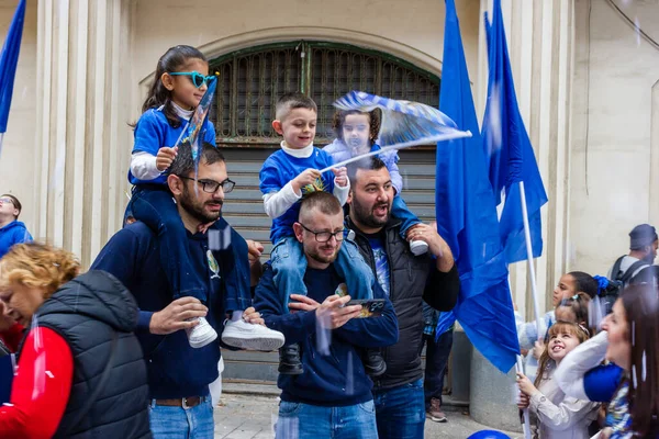 Cospicua, Malta - November 30th, 2025, Vibrant Street Parade With Blue And White Balloons, Flags, And Crowds Celebrating Festival