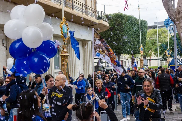 Cospicua, Malta - November 30th, 2025, Vibrant Street Parade With Blue And White Balloons, Flags, And Crowds Celebrating Festival