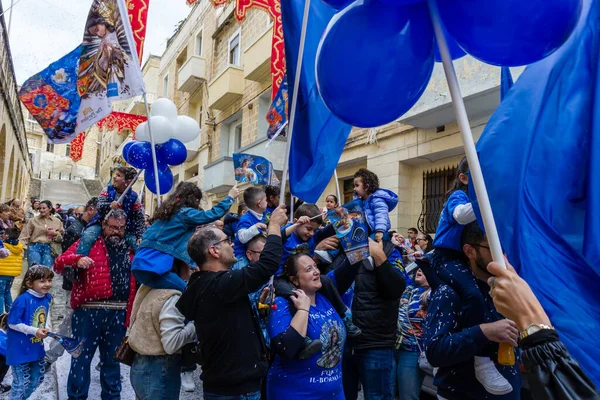 Cospicua, Malta - November 30th, 2025, Vibrant Street Parade With Blue And White Balloons, Flags, And Crowds Celebrating Festival