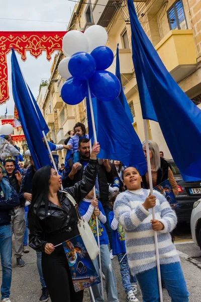 Cospicua, Malta - November 30th, 2025, Vibrant Street Parade With Blue And White Balloons, Flags, And Crowds Celebrating Festival
