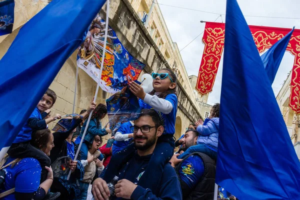Cospicua, Malta - November 30th, 2025, Vibrant Street Parade With Blue And White Balloons, Flags, And Crowds Celebrating Festival