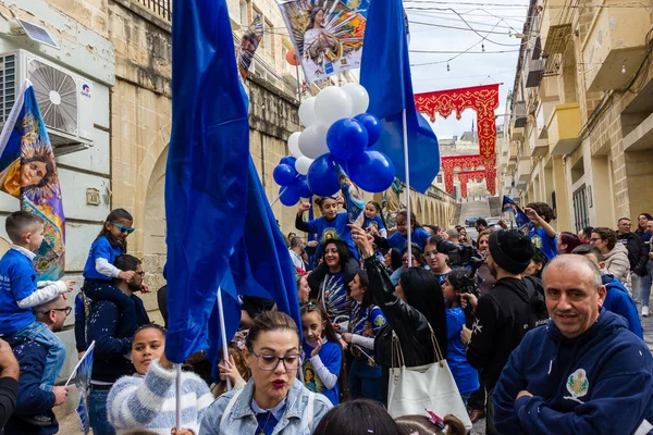Cospicua, Malta - November 30th, 2025, Vibrant Street Parade With Blue And White Balloons, Flags, And Crowds Celebrating Festival
