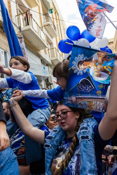 Cospicua, Malta - November 30th, 2025, Vibrant Street Parade With Blue And White Balloons, Flags, And Crowds Celebrating Festival