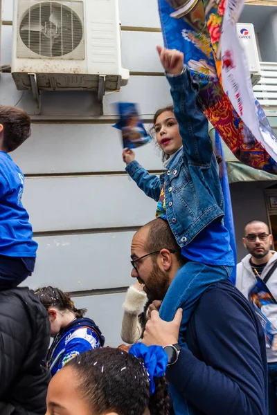 Cospicua, Malta - November 30th, 2025, Joyful Family Parade With Child On Man's Shoulders Amid Colorful Banners And Crowd