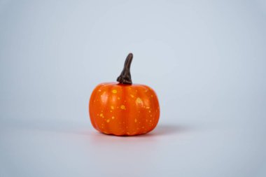 Beyaz bir yüzeyde izole edilmiş küçük turuncu bir balkabağının basit fotoğrafı. Sonbahar, hasat, Cadılar Bayramı tasarımları, mevsimlik kartlar ya da ev dekorasyonu reklamları için mükemmel.. 