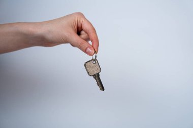 Minimalist image of a hand holding a key on a neutral background. Perfect for real estate, property rental, home ownership, mortgage, or security service advertisements. 