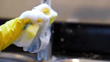 Extreme close-up of hands in yellow gloves cleaning the hot-cold faucet handle with foamy sponge. Perfect for home cleaning, hygiene, and professional cleaning service visuals. 