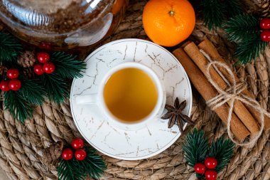 Turuncu ve şenlikli çam desenli beyaz bardakta sıcak çay. Doğal ışıklandırmalı rahat Noel kompozisyonu.