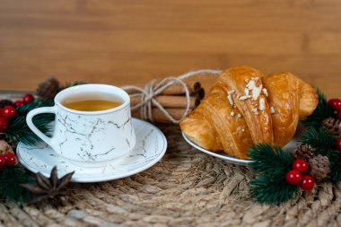 Çam dalları ve Noel dekoruyla örülmüş bir fincan çay ve kruvasan. Sıcak bir sabah ve tatil havası.. 
