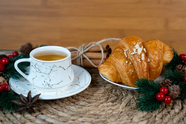 Çam dalları ve Noel dekoruyla örülmüş bir fincan çay ve kruvasan. Sıcak bir sabah ve tatil havası.. 