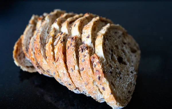 Siyah yüzey üzerinde çıtır çıtır kabuklu köy kepekli ekmek. Sağlıklı yaşam tarzı görselleri için estetik minimal yemek fotoğrafı.