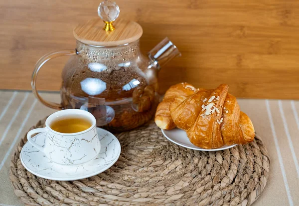Tahta bir yüzeyde bir fincan çay ve taze kruvasan. Doğal gün ışığında minimum konforlu kahvaltı. 
