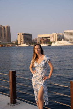 Modern şehir arka planına sahip su kenarında poz veren manken. Doğal zarafet ve şık kıyafet şık bir yaz havası yaratır.. 
