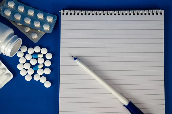 Kırmızı-mavi arka plan üzerinde kalem ve haplar bulunan defter, reçeteyi ve teletıp kavramlarını sembolize ediyor. 