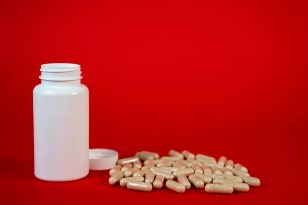 Kırmızı arka planda bej kapsüllü beyaz plastik şişe. İlave, eczane veya tıbbi pazarlama kavramları için mükemmel. Yüksek kalite fotoğraf