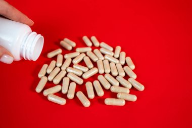 Kırmızı arka planda bir yığın kapsül oluşuyor. İlaç üretimi, sağlık takviyeleri ve günlük ilaç kavramı. 