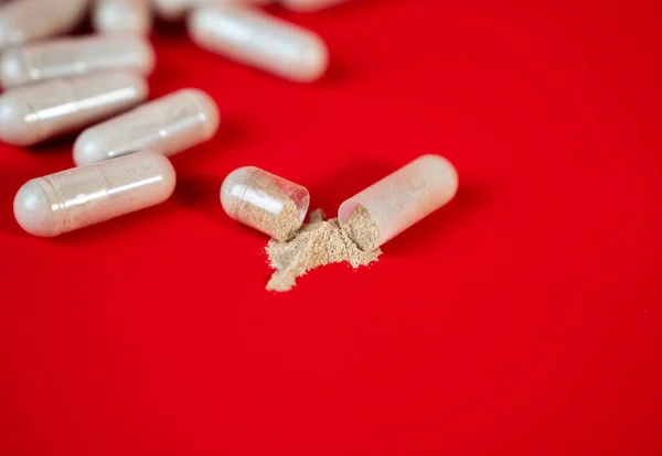 Kırmızı zemin üzerine toz dökülmüş açık kapsül. Dozajı, malzemeleri ya da ilaç kalitesini sembolize eden ilaç ve takviye konsepti. 
