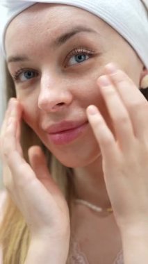 Yüzüne ve boynuna krem sürdükten sonra parmak uçlarıyla hafifçe dokunan gülümseyen bir kadının yakın çekimi. Rahatlamış ve mutlu ifade, cilt bakımı memnuniyeti, özgüven ve sağIık kavramı. 