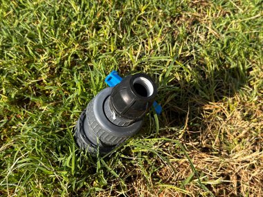 Bahçe sulama konnektörü ve fıskiye başlığı yeşil çimenlerin üzerinde, açık deniz erişimi konsepti, hortum montajı ve manzara bakımı. 