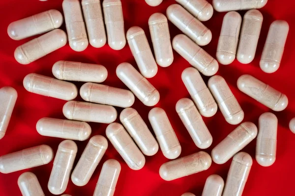 Kırmızı yüzeye saçılmış kapsüllerin makro yakın çekimi. İlave veya vitamin kavramları için modern ilaç fotoğrafı. 