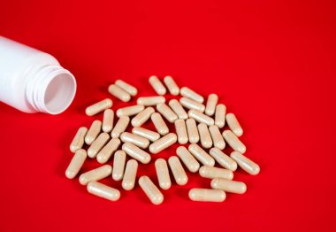 Kırmızı yüzeyde beyaz bir şişeden kapsüller dökülüyor. İlave dozaj, sağlık hizmeti rutini ve ilaç tasarımı kavramı. 