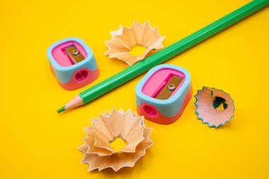 Kıvrımlı talaşlarla çevrili yeşil kalem ve sarı arka planda çift tonlu bileyici. Okul ve yaratıcı temalar için harika. 