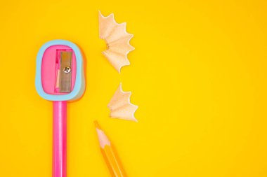 Kıvrımlı kalem talaşı ve sarı arka planda küçük parçalar olan izole edilmiş bir keskinleştirici. Temiz ve asgari kırtasiye bileşimi.