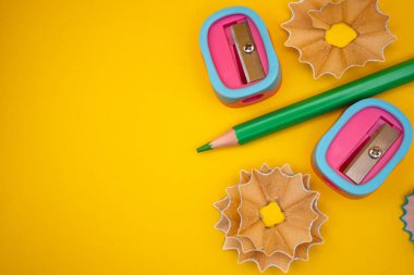 Renkli bir keskinleştiricinin yakın plan düz yatağı ve parlak sarı bir zemin üzerinde birden fazla büyük kalem talaşı. Yaratıcı kırtasiye konsepti. 