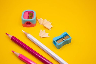 Düz pembe beyaz kalemler, mavi kalemler ve parlak sarı bir yüzey üzerinde talaşlar. Eğitim, sanat ve yaratıcı okul temaları için mükemmel. 
