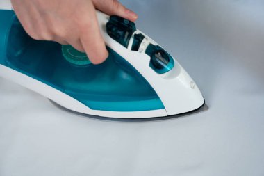 Buhar ütüsü beyaz kumaşa baskı yapıyor, yakın çekim. Giysi bakımı, çamaşır rutini ve ev işleri kavramı.. 