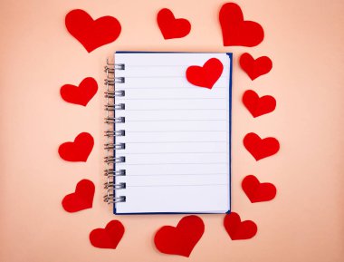 Tarafsız arkaplanda kırmızı kalpler tarafından çerçevelenmiş boş sayfalı bir defter aç. Aşk mesajları, notlar, davetiyeler ve romantik tasarımlar için sevgililer günü modeli.