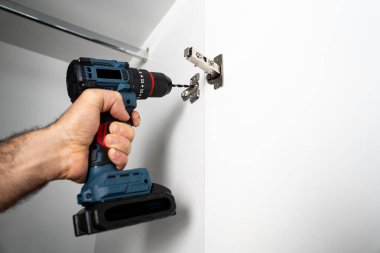 Kablosuz matkap kullanarak duvara metal menteşe takan bir tamircinin yakın çekimi. Ev yenileme ve mobilya montaj kavramı.