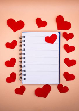 Yumuşak bej arka planda kırmızı kağıt kalplerle çevrili dikey defter. Romantik mesajlar için fotokopi alanı olan Sevgililer Günü modeli.