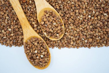 Açık arkaplanda iki tahta kaşıkla karabuğday homurdanır. Doğal gıda konsepti, sağlıklı tahıl bileşeni ve minimum bileşim.