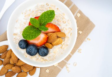 Taze meyve ve fındıklı beyaz bir kase sağlıklı yulaf ezmesinin dokulu bir peçeteye yerleştirilmiş hali. Lezzetli ve görsel olarak çekici bir kahvaltı. Yüksek kalite fotoğraf