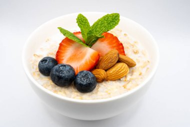 Çilek, yaban mersini, badem ve nane yapraklarıyla süslenmiş sağlıklı yulaf ezmesiyle dolu beyaz bir kâseye yakın plan. Güne mükemmel bir başlangıç. Yüksek kalite fotoğraf